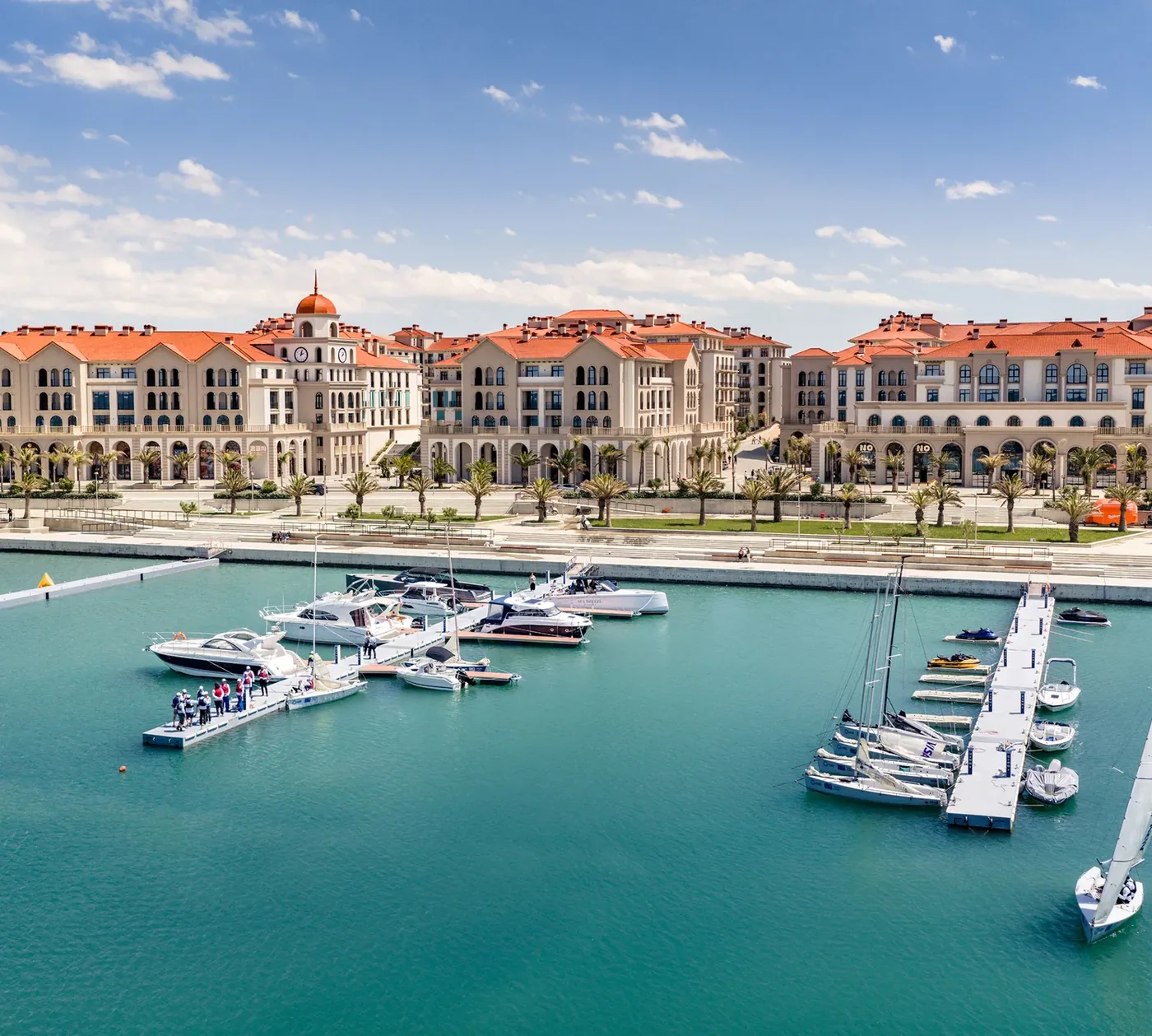 Гавань с воды: понтоны с яхтами, за ними набережная и дома Marina Village с аркадой первых этажей