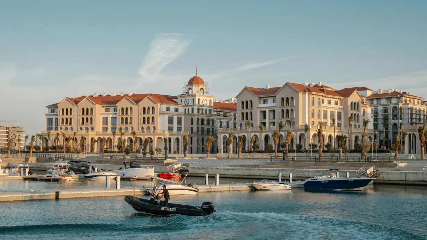 Катер идёт по гавани мимо набережной и домов Marina Village